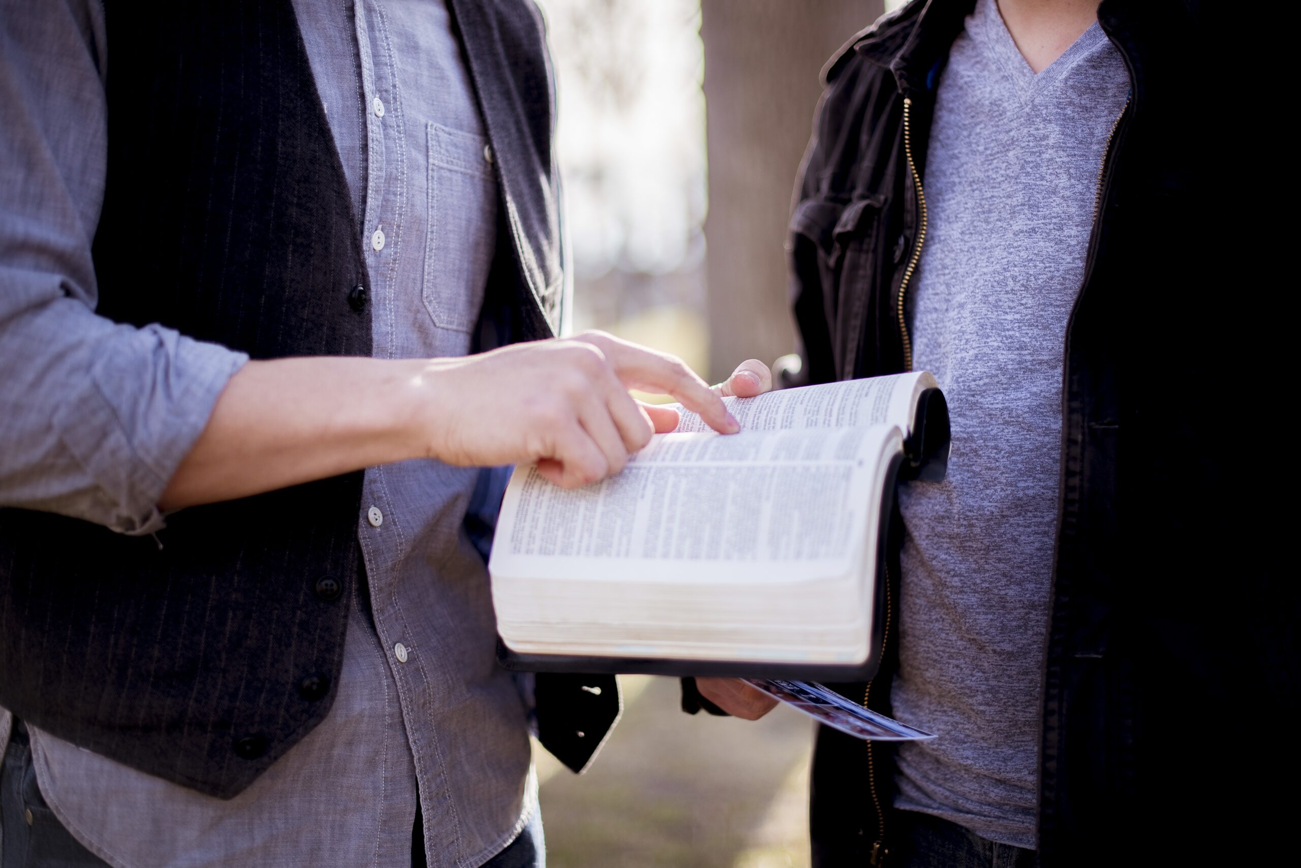 A closeup shot of a male pointing to a sentence in the bible with a blurred background